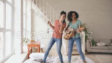 混合种族<strong>的</strong>年轻滑稽女孩跳舞，用吹风机唱歌，在床上弹声吉他。 <strong>姐妹们</strong>玩得开心